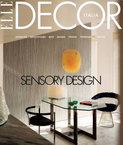 Front cover of ELITE DECOR ITALIA magazine featuring a modern interior scene with a glass table, black chairs, a warm yellow pendant light, and the headline 'SENSORY DESIGN'.