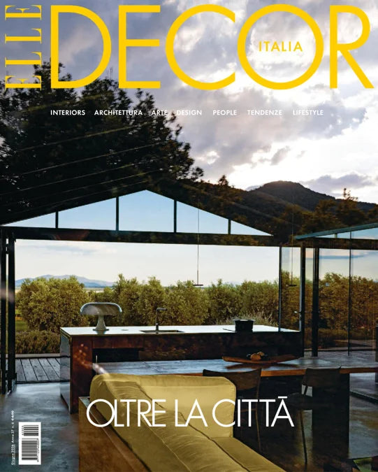 The Decor Italia magazine cover featuring a modern glass kitchen structure overlooking a lush green landscape with mountains in the background. The title 'THE DECOR ITALIA' is displayed in bold yellow text at the top, and the subtitle 'OLTRE LA CITTÀ' is written at the bottom.